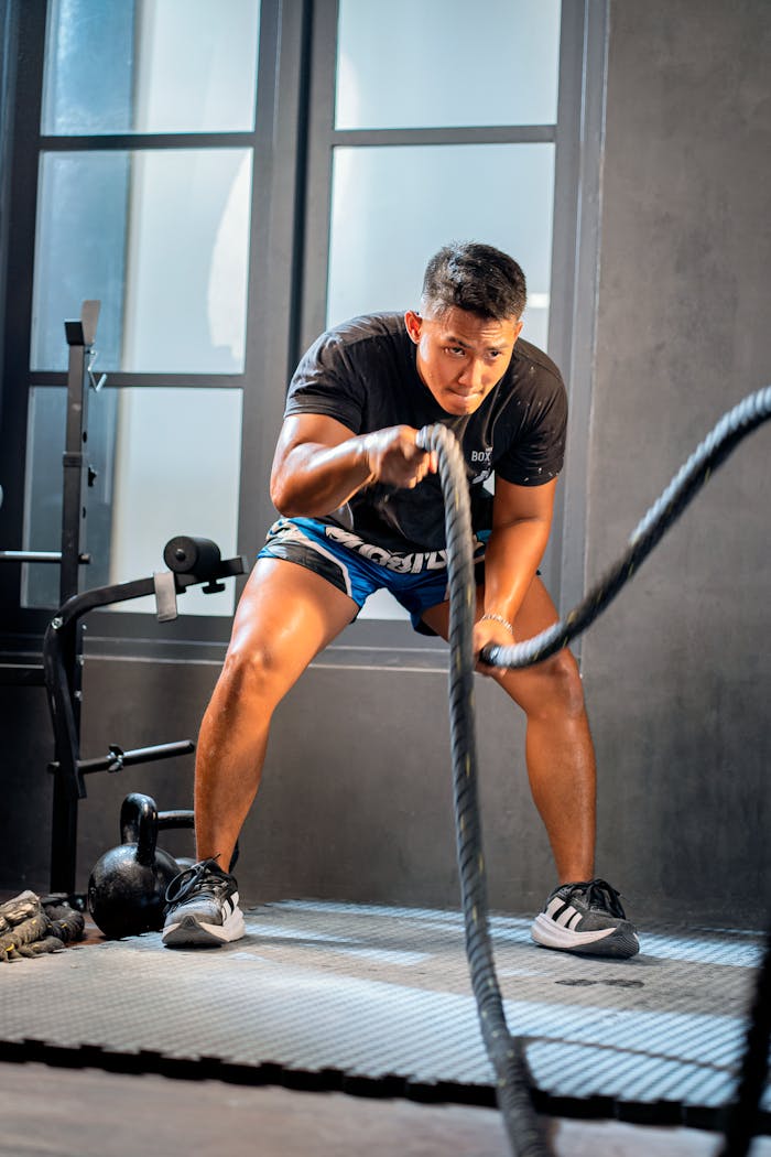 Focused athlete training with battle ropes in a gym setting, enhancing strength.