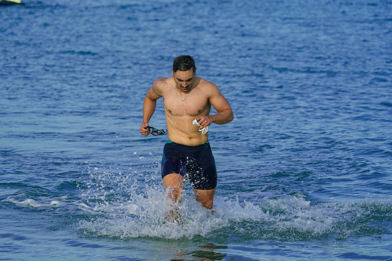 A fit man running out of the sea at Kuşadası beach, showcasing fitness and joy.